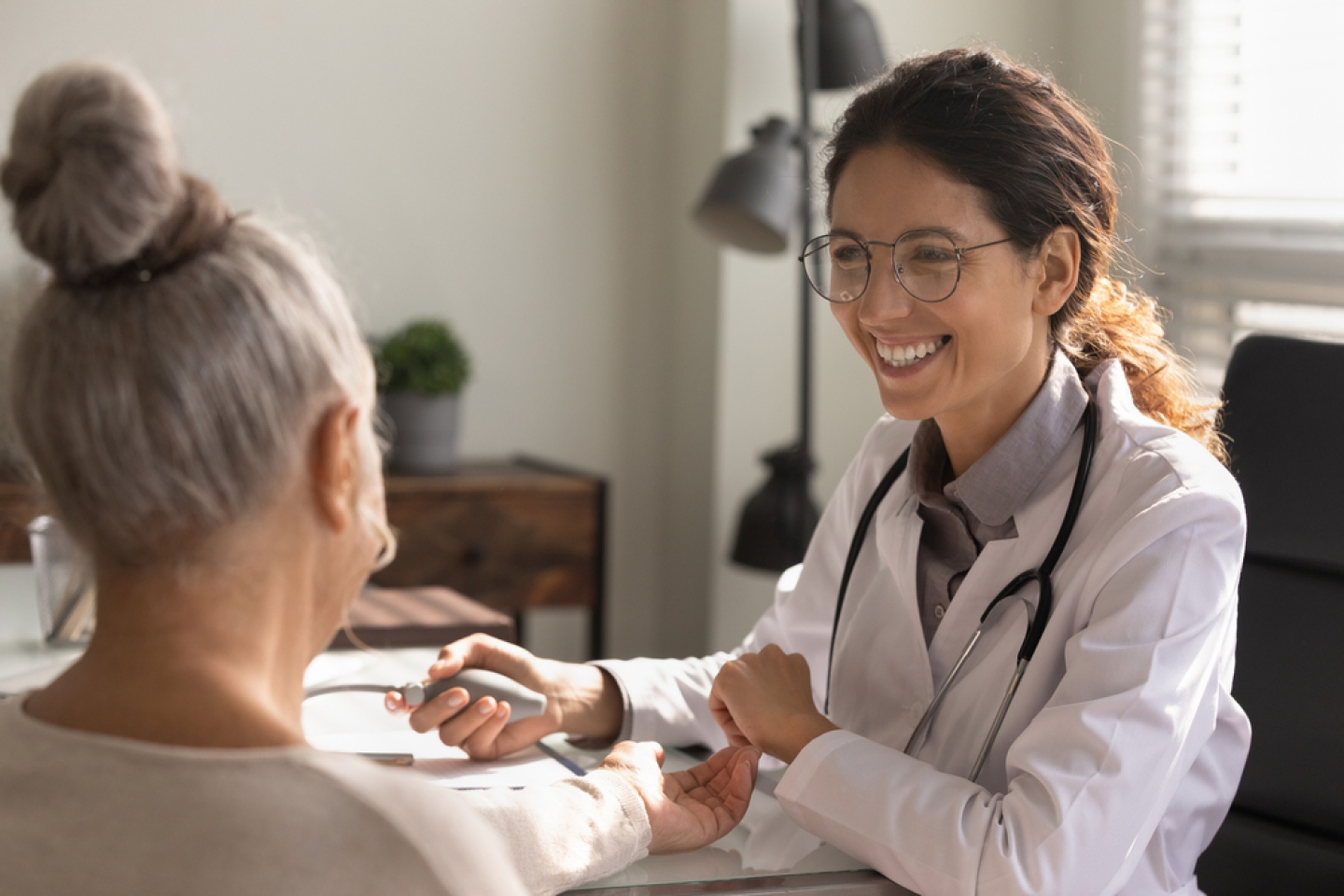 Close up smiling female doctor wearing glasses checking old woman blood pressure at meeting in hospital office,