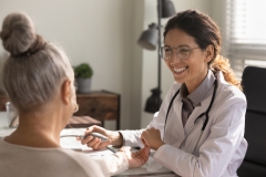 Close up smiling female doctor wearing glasses checking old woman blood pressure at meeting in hospital office,