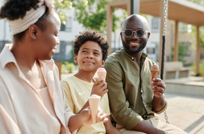 Happy African American family eating ice cream together outdoors while sitting on the swing